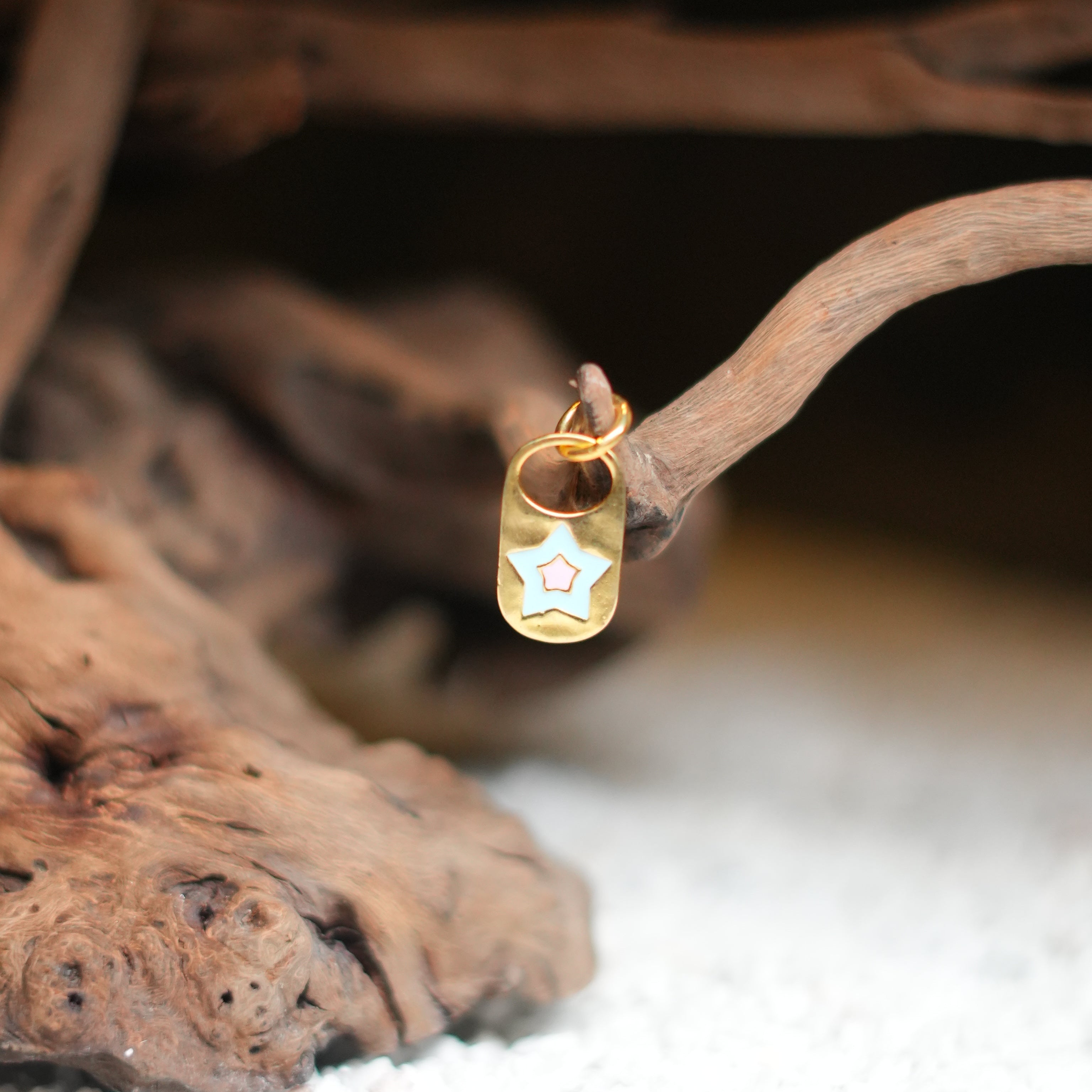 A gold-colored charm with a star shape pendant, resembling an evil eye, placed against a natural, rustic background with wooden elements.