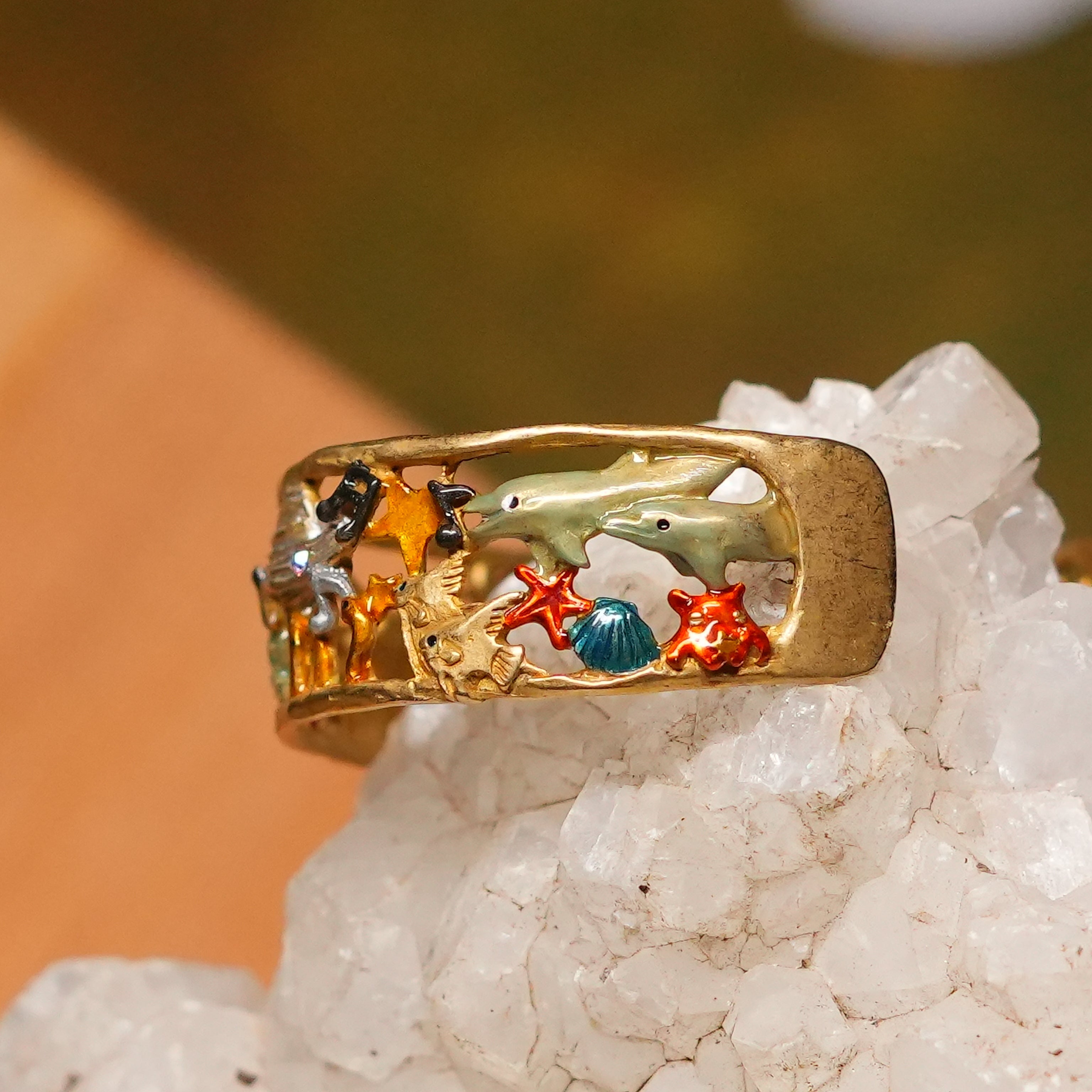 A multicolored bangle bracelet with gold-colored brass, adorned with cut glass in various shapes including stars and planets, and featuring a pattern with an astronaut and dolphins.