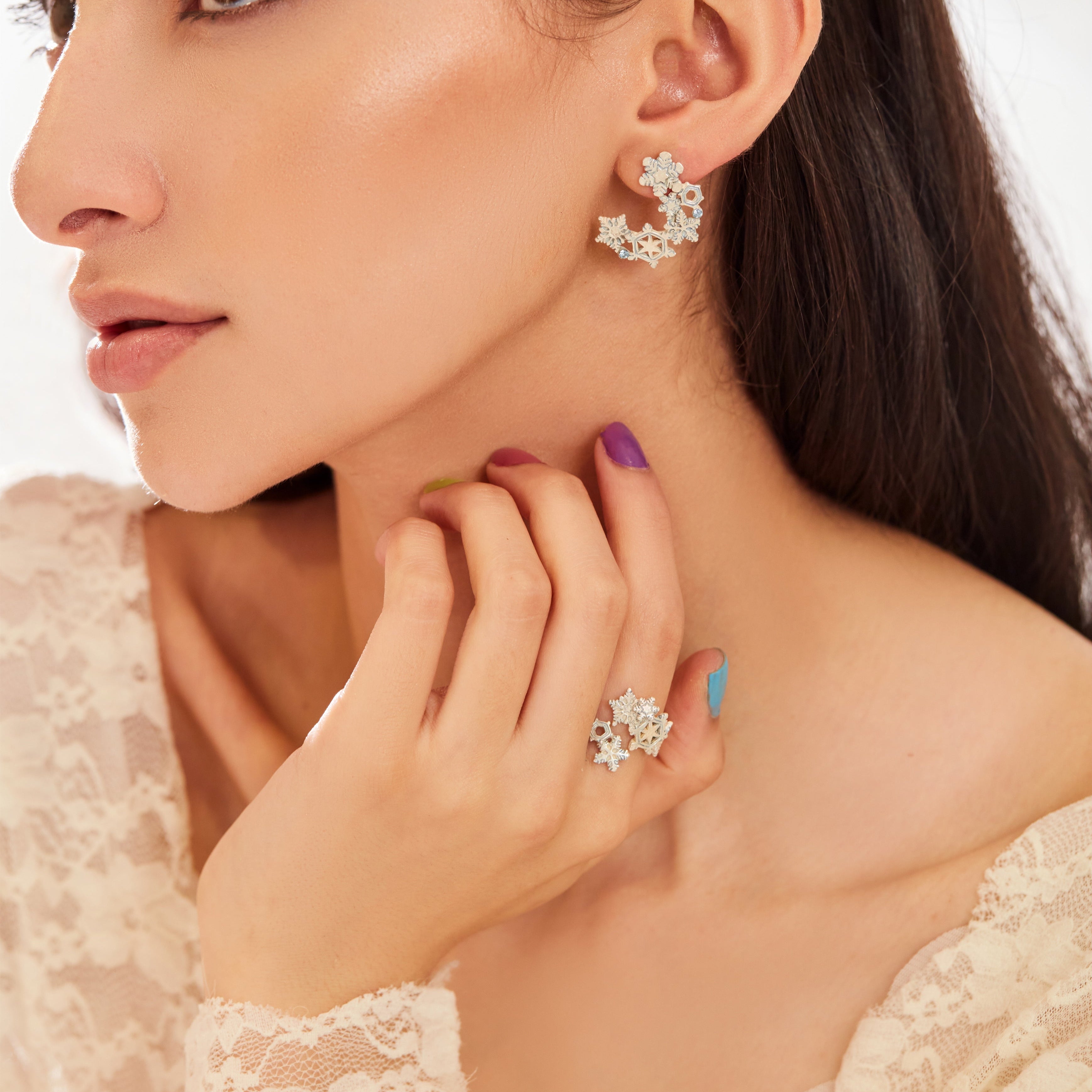 A silver-colored brass ring with snowflake-like patterns, accompanied by a similar earring, against a white background.