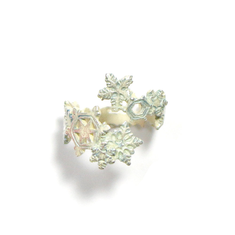 A silver-colored brass ring with snowflake-like patterns, accompanied by a similar earring, against a white background.