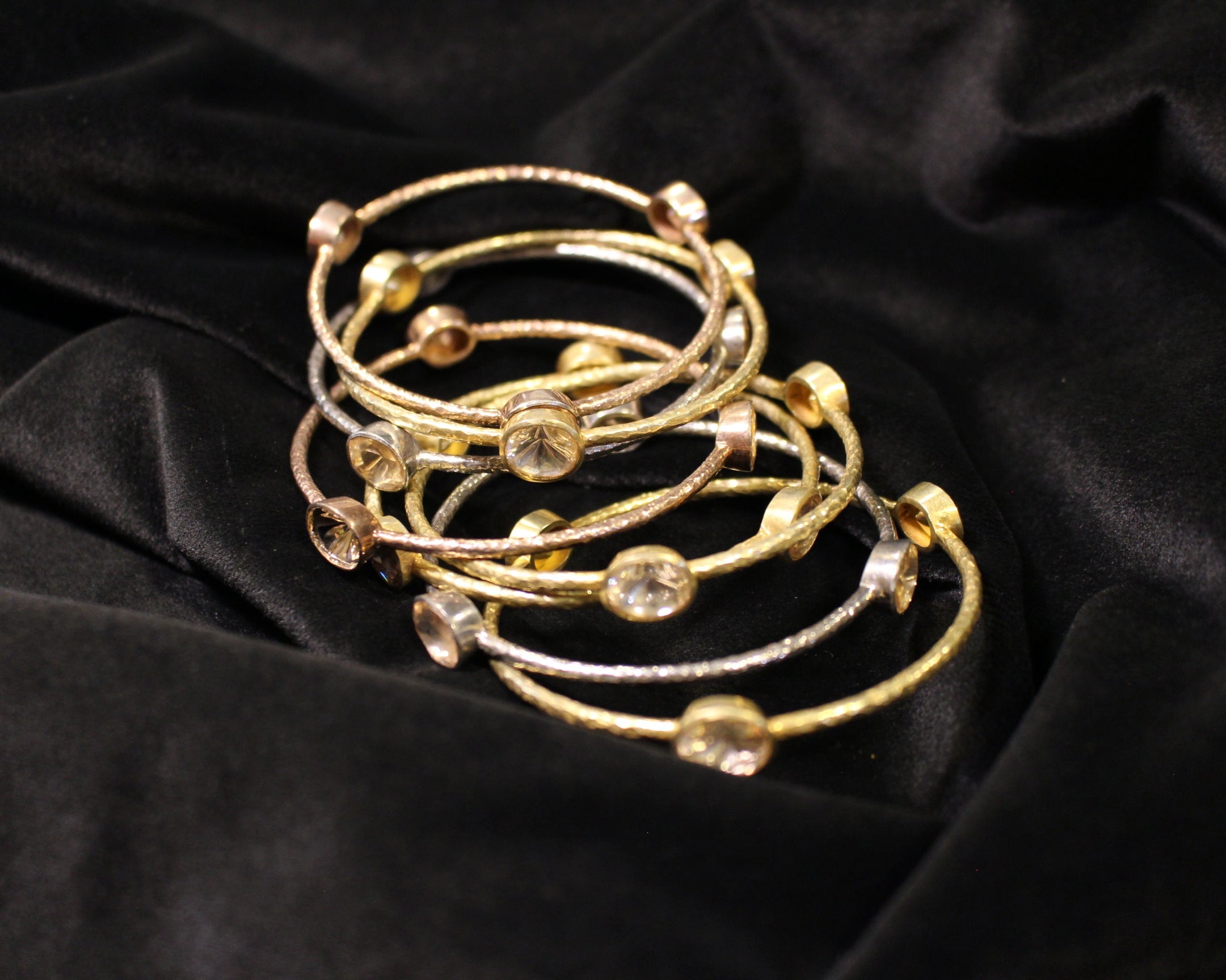 Set of gold bracelets with gemstones on a black fabric background