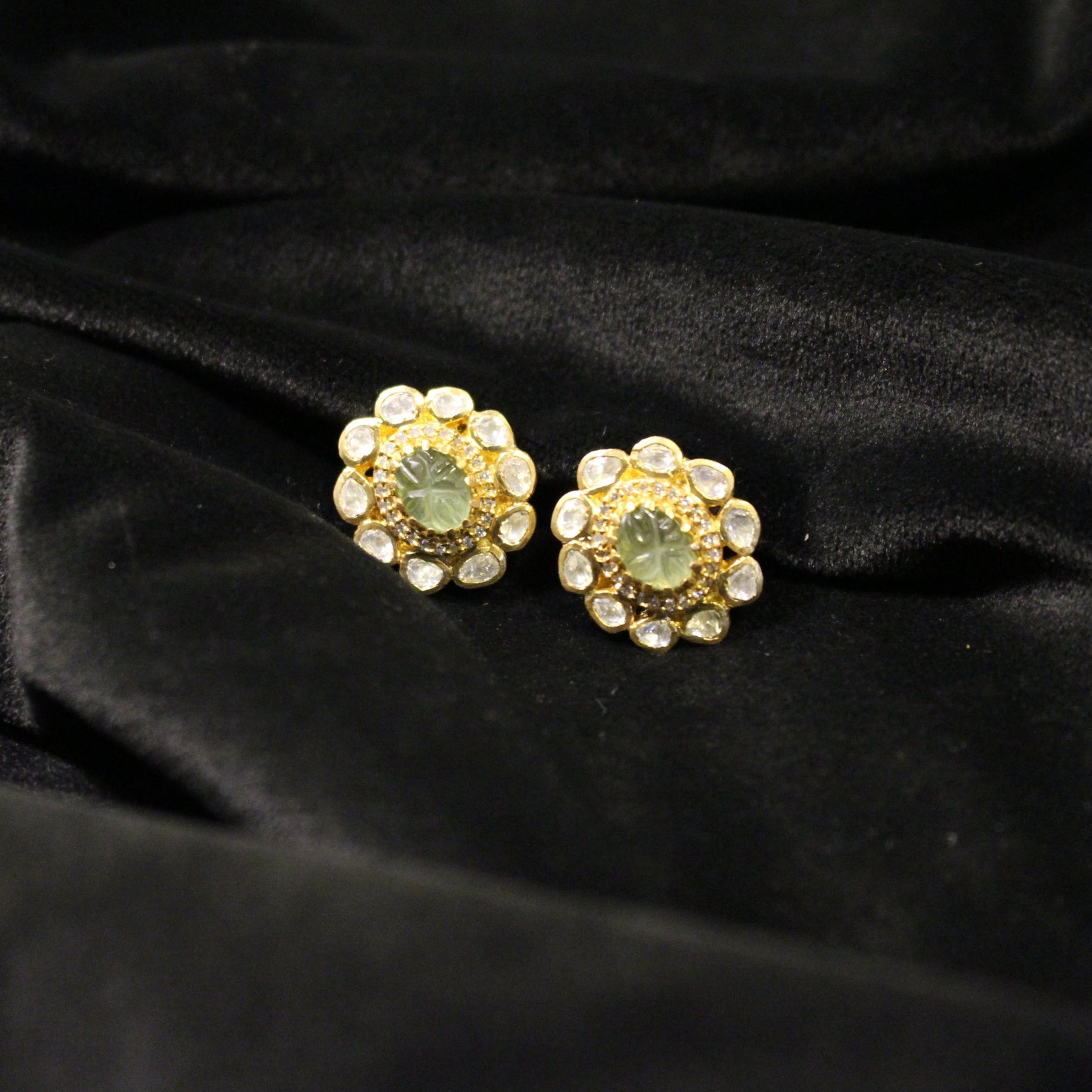 Gold earrings with green gemstones on a black velvet background