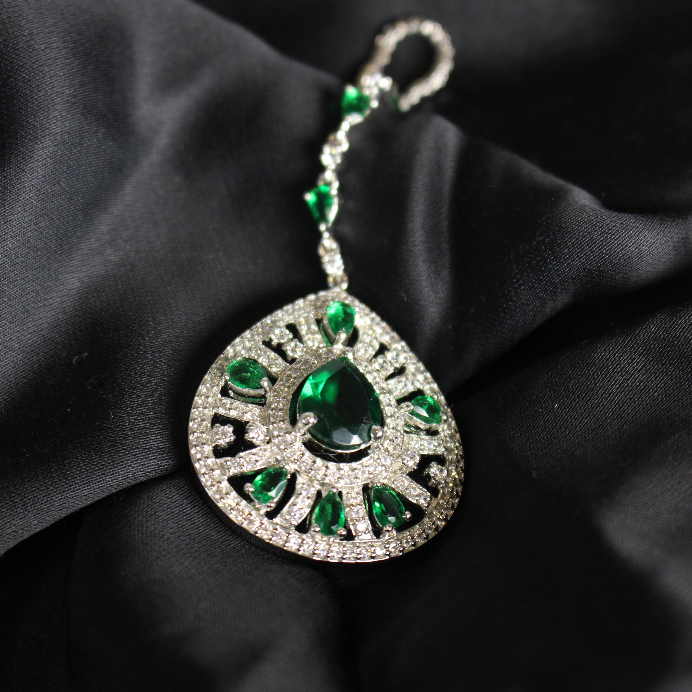 Jewelry pendant with green gemstones on a black fabric background